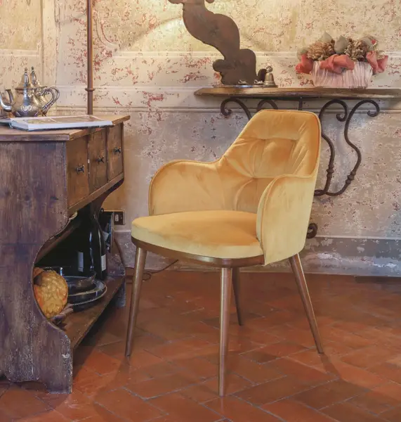 Mustard velvet Rise Armchair with tufted back and wooden legs, positioned beside a vintage wooden cabinet.