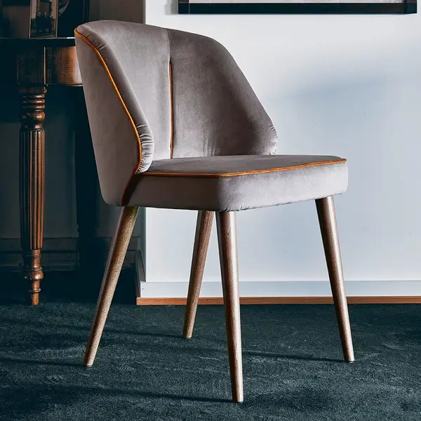 Angled view of the Alissa side chair in gray upholstery with wooden legs, featuring a cushioned seat and back with piping.