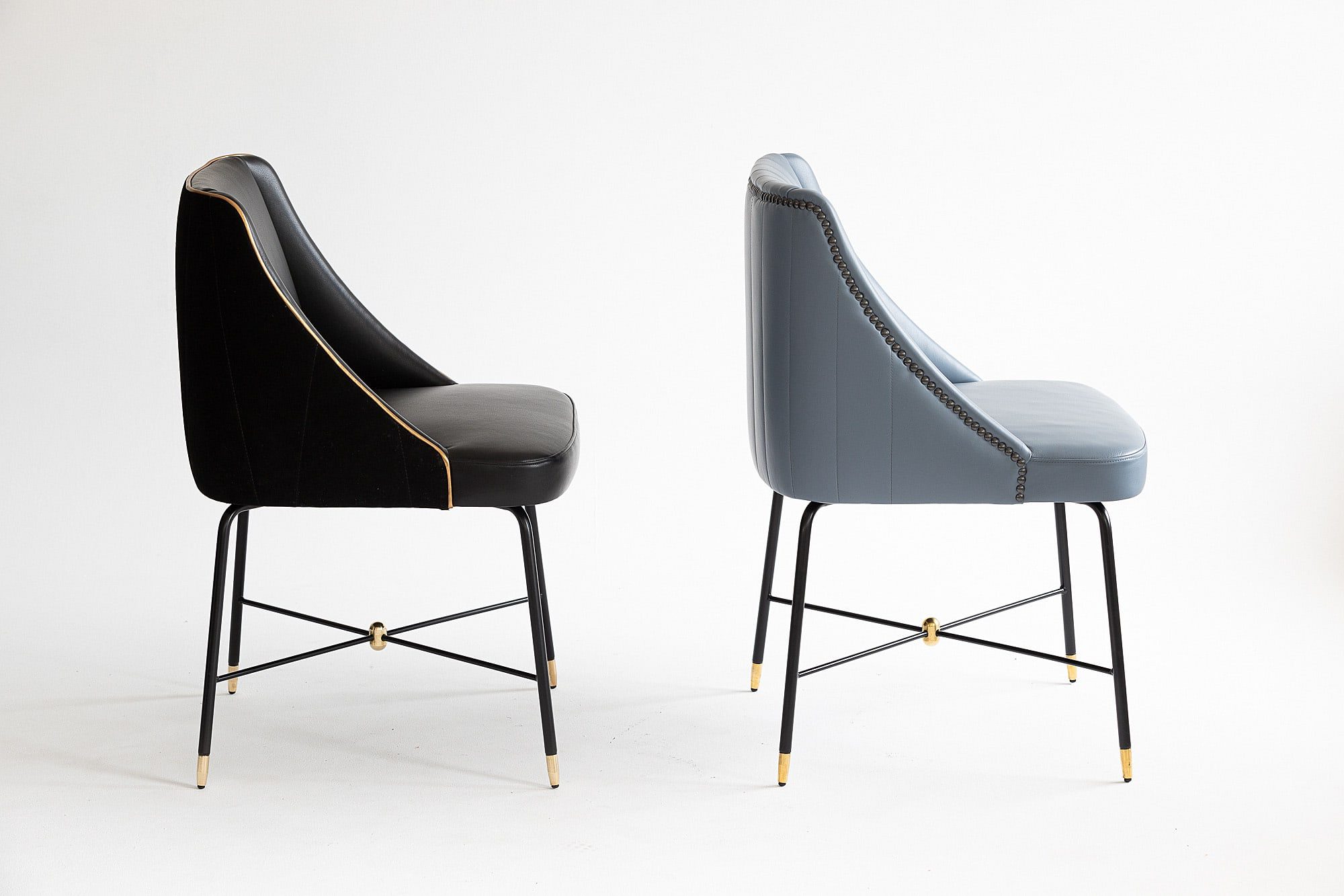 Side view of a black and a blue Soho Armchair. Both have metal frames and upholstered seats and backs.