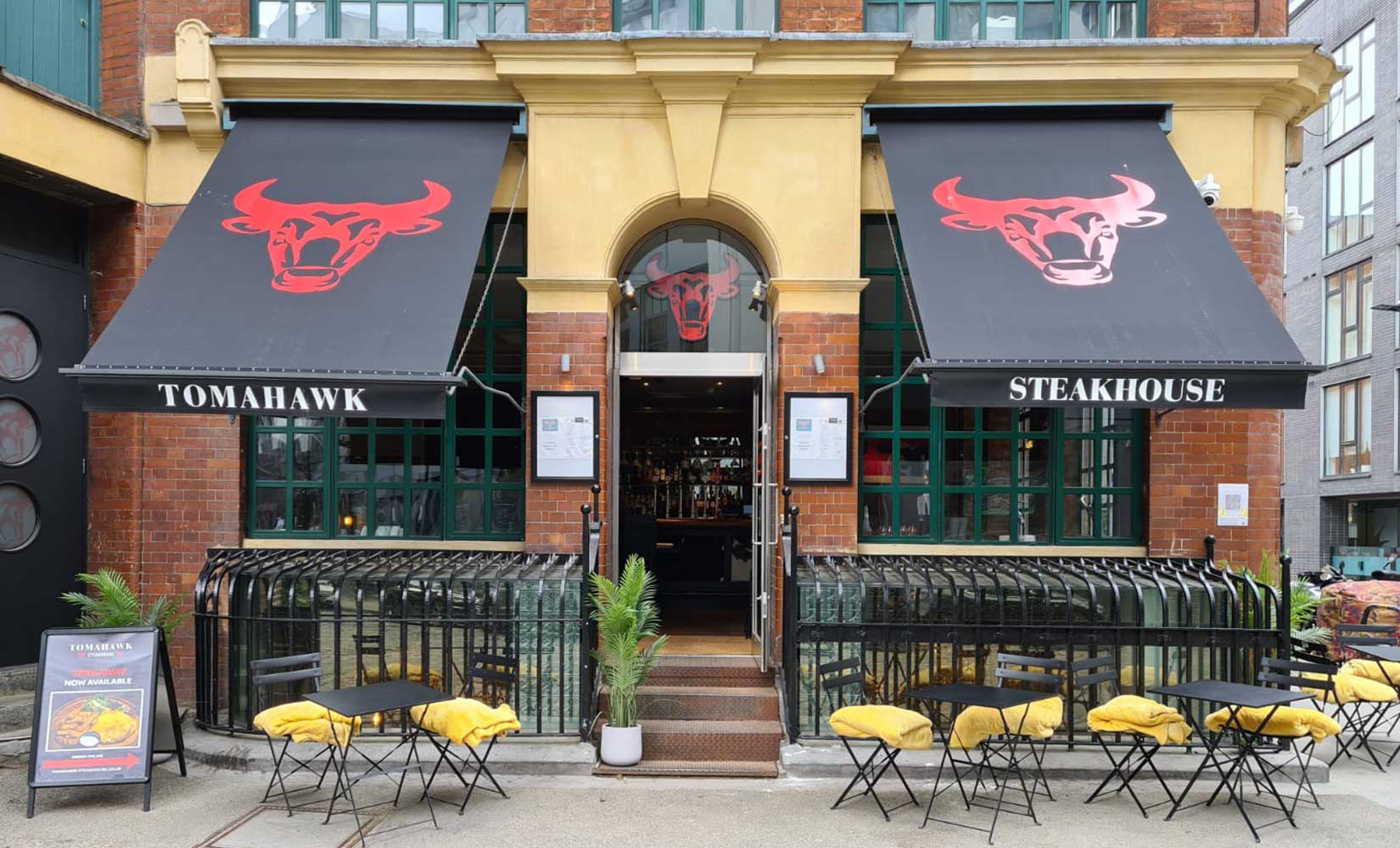 Tomahawk Steak House in Hoxton. Restaurant exterior with outdoor seating and bull logo on awnings.
