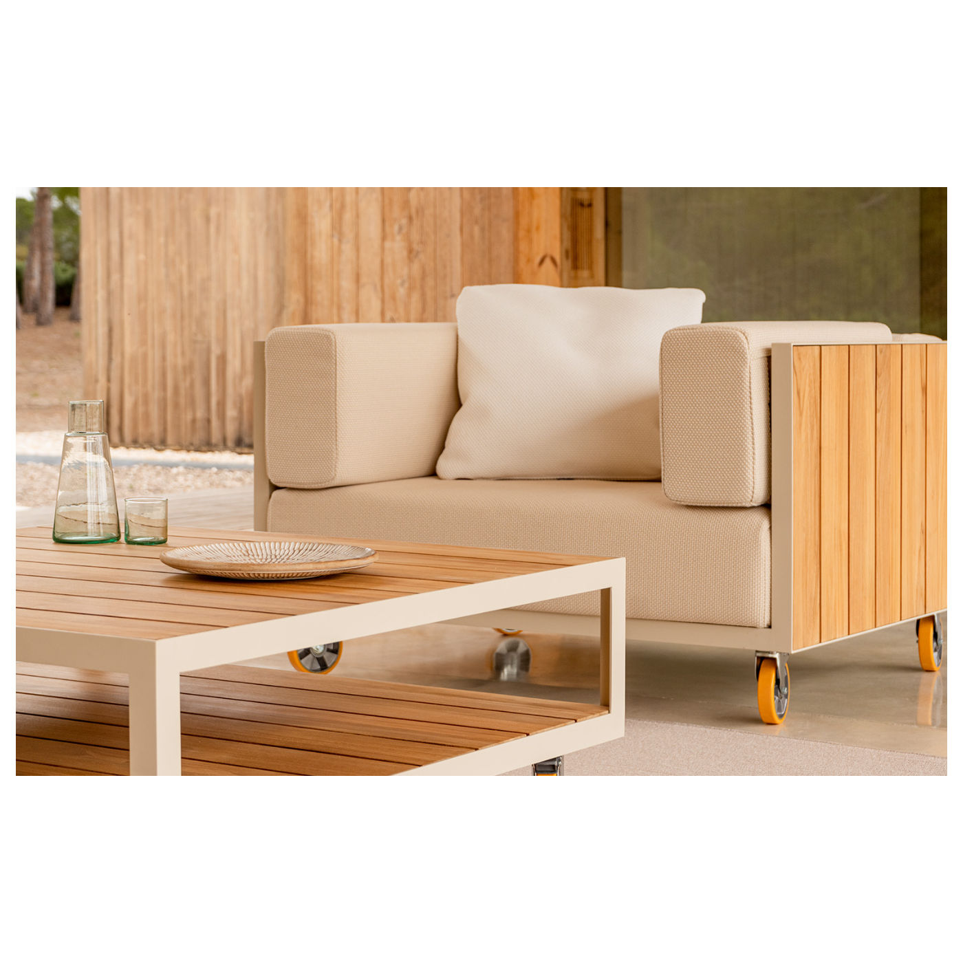 Upholstered Vineyard lounge chair with a metal frame and teak wood detailing. The chair has castors and a matching coffee table.