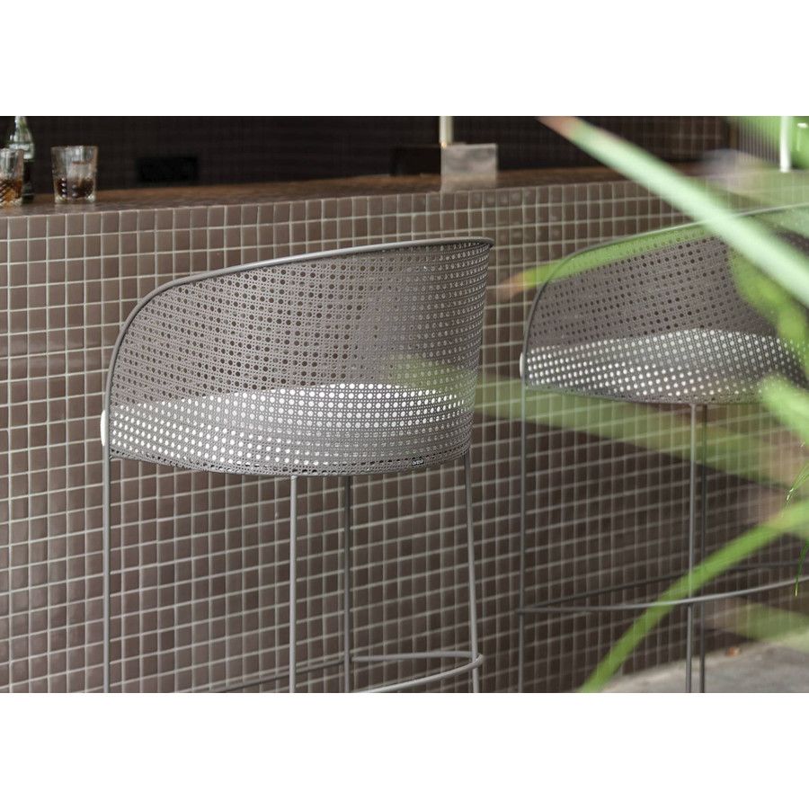 Arena barstool with perforated mesh back and sled base, placed against tiled wall on outdoor patio.