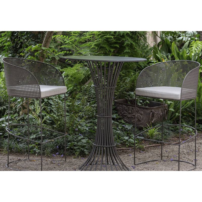 Pair of Arena barstools with light cushions and curved mesh backs, set beside a round metal table amid lush garden greenery.