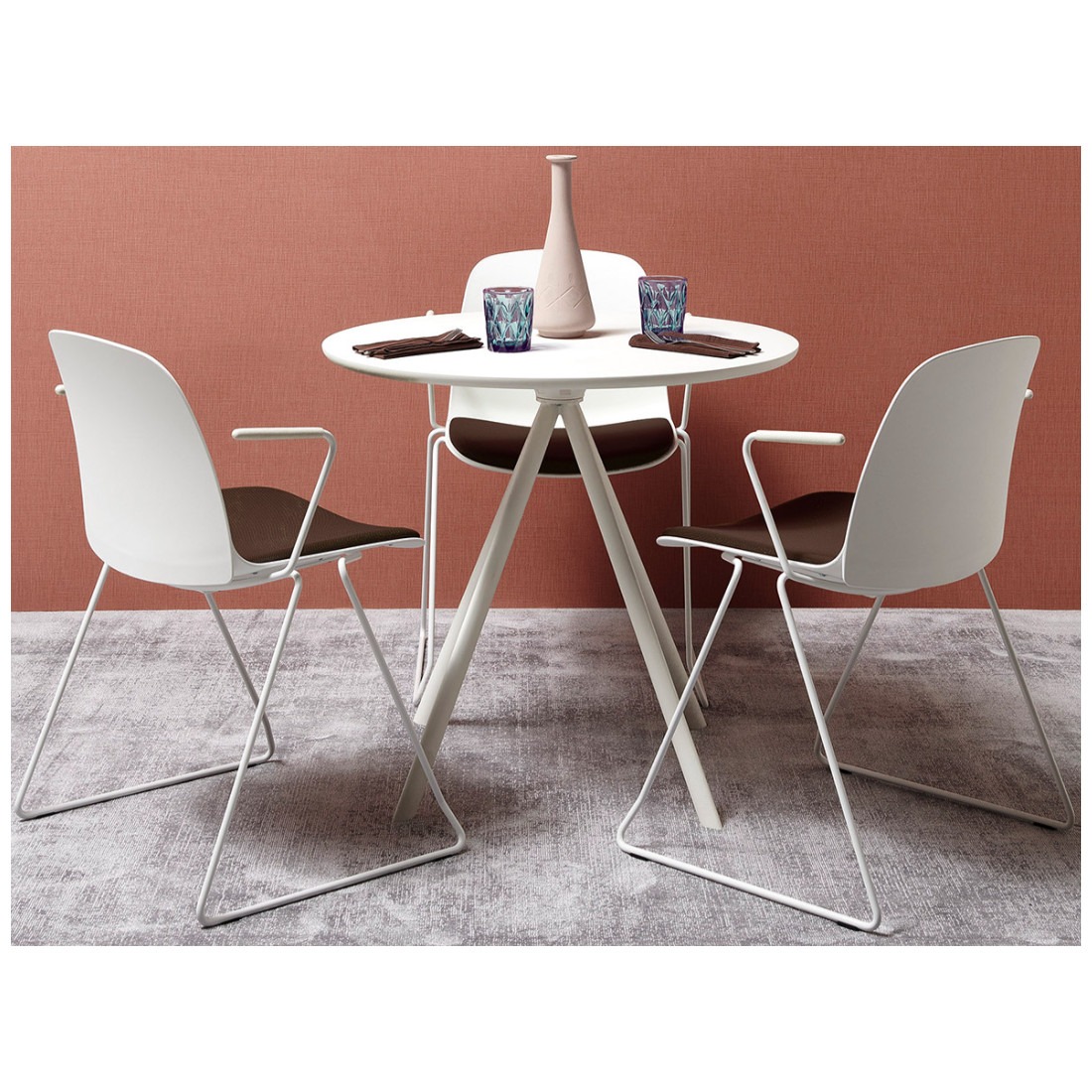 Three white Kire sled armchairs with brown upholstered seat pads around a white table.