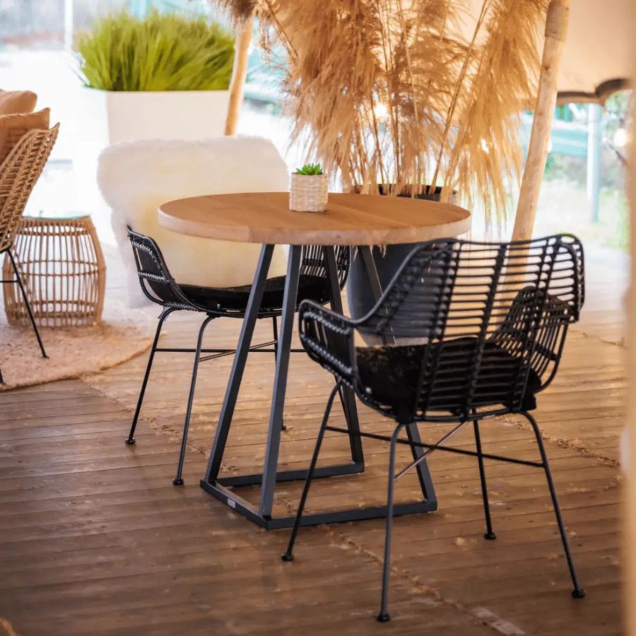 Two black Palm armchairs with metal frames and woven seats around a wooden table on a wooden floor.