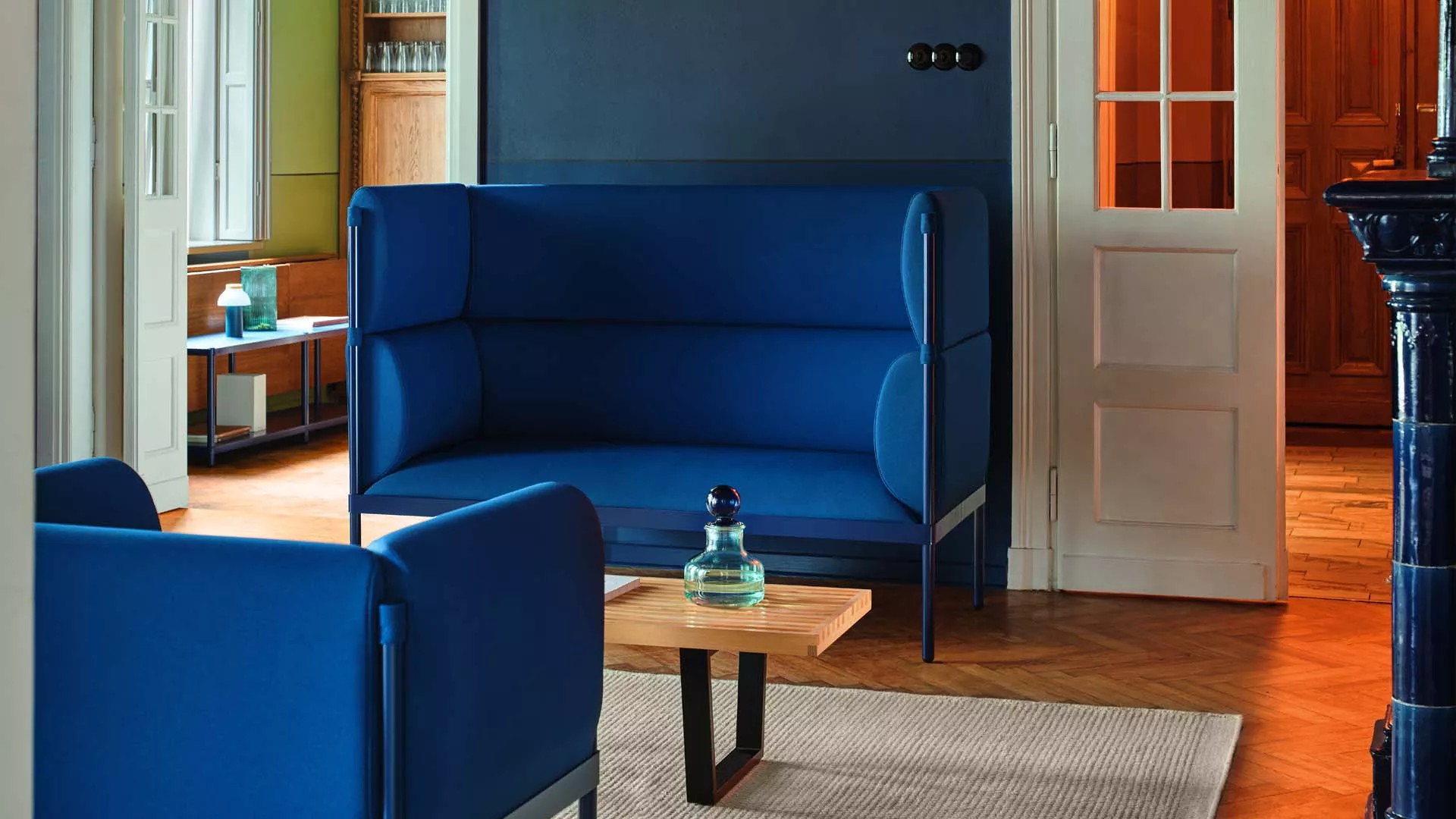 stilt sofa Blue Stilt 3 Seater Sofa with a metal frame and upholstered seat. The high-back sofa is in a lounge setting with a small table.