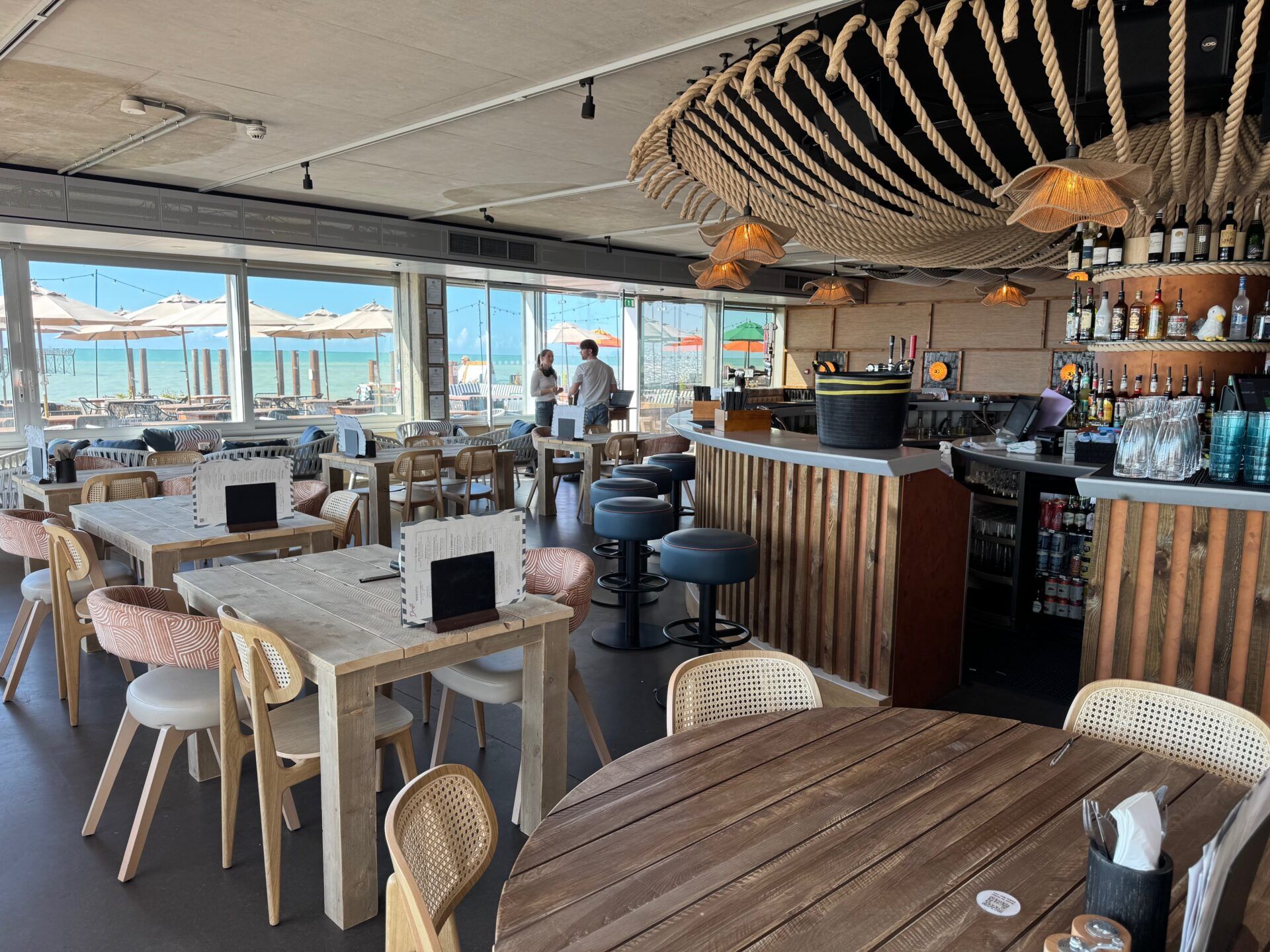Drift Bar & Kitchen Brighton Drift Bar & Kitchen, Brighton. Interior view of coastal restaurant with tables, chairs, bar, and seaside view.