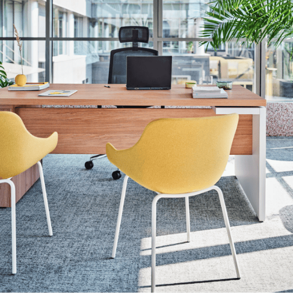 Angled view of a yellow Baltic Classic M Armchair with white legs, in an office setting, showcasing its upholstered seat.