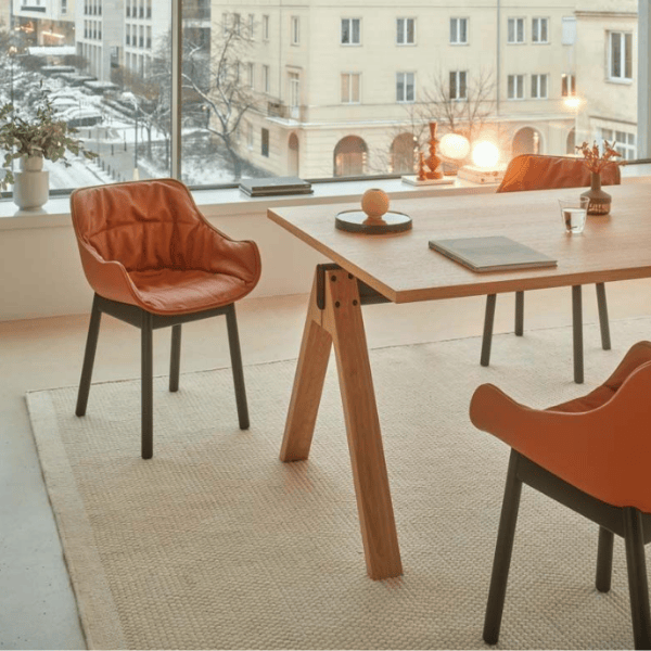 Close-up of Baltic Soft W Armchair in orange leather, showcasing its soft curves, integrated arm support, and slim black legs.