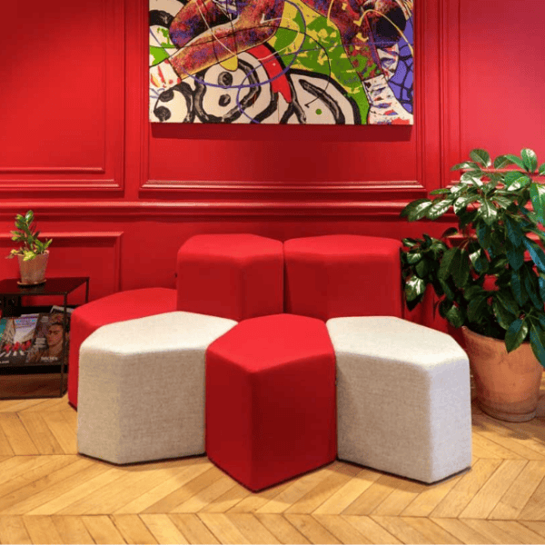 Eye-level shot featuring red and white Bazalto Poufs arranged in a hexagonal pattern, set against a red wall with abstract art.