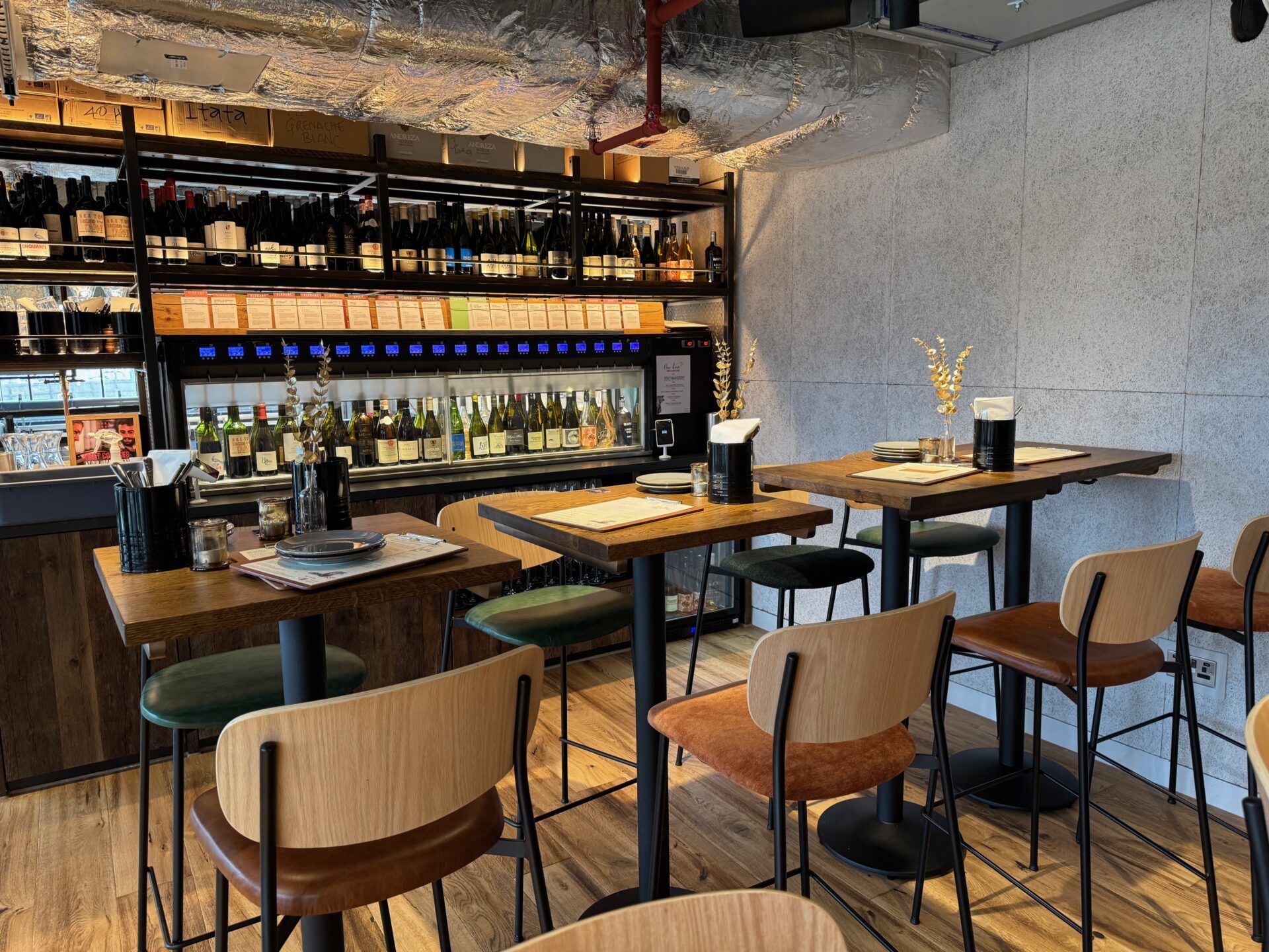 Vagabond Urban Winery London interior: Tables, chairs, and wine rack filled with bottles. Wine tasting experience.