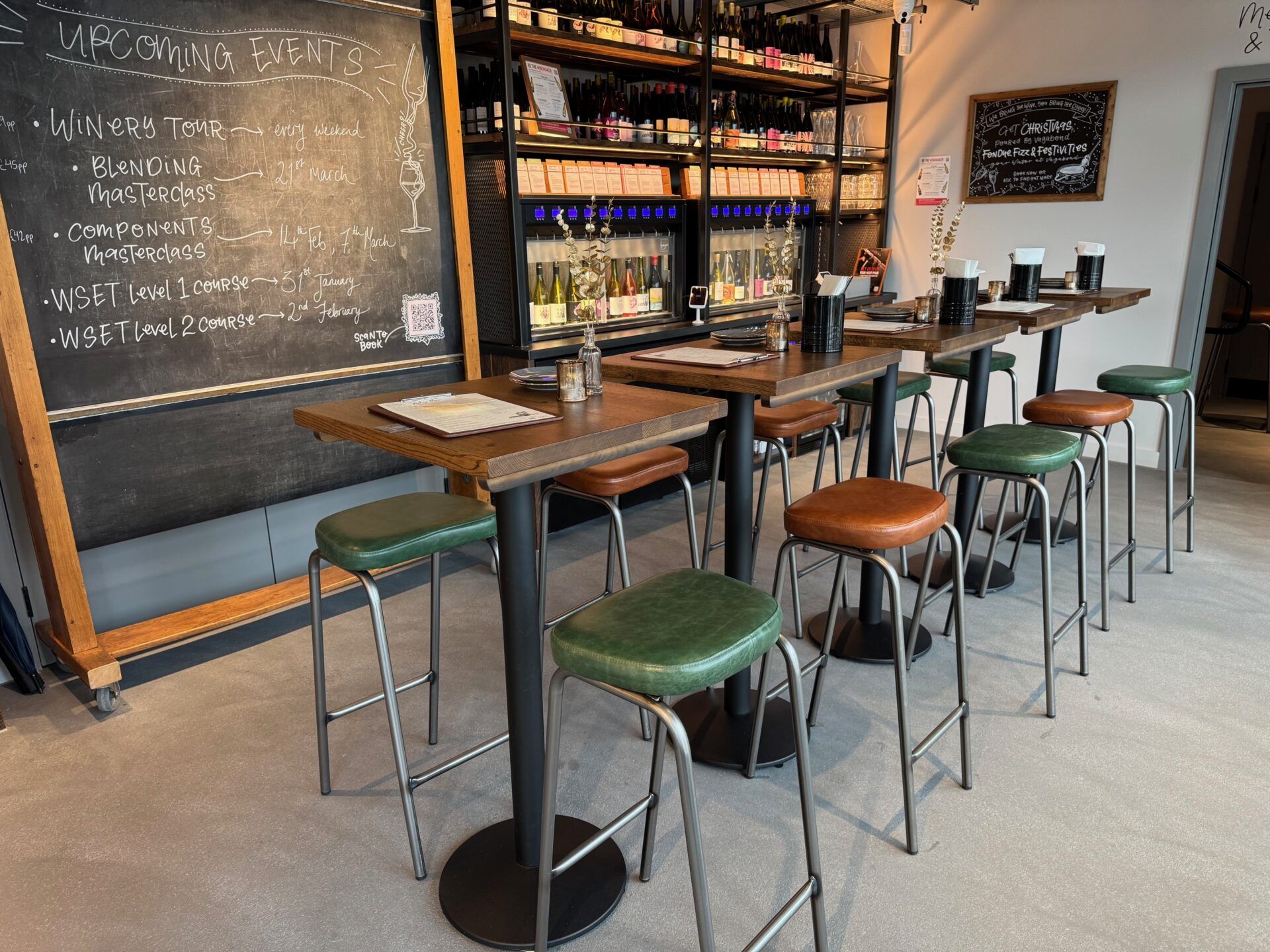 Vagabond Urban Winery in London: Interior view of tasting tables and stools, wine racks, and upcoming events chalkboard.