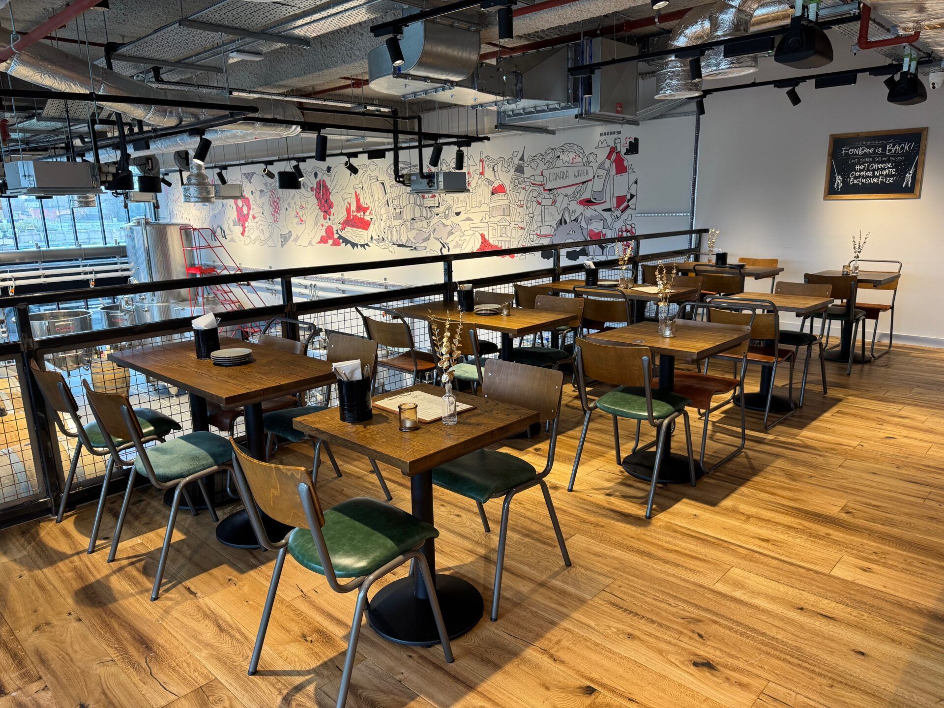 Vagabond Urban Winery London interior with tables, chairs, mural, and brewing equipment visible. Modern, industrial design.