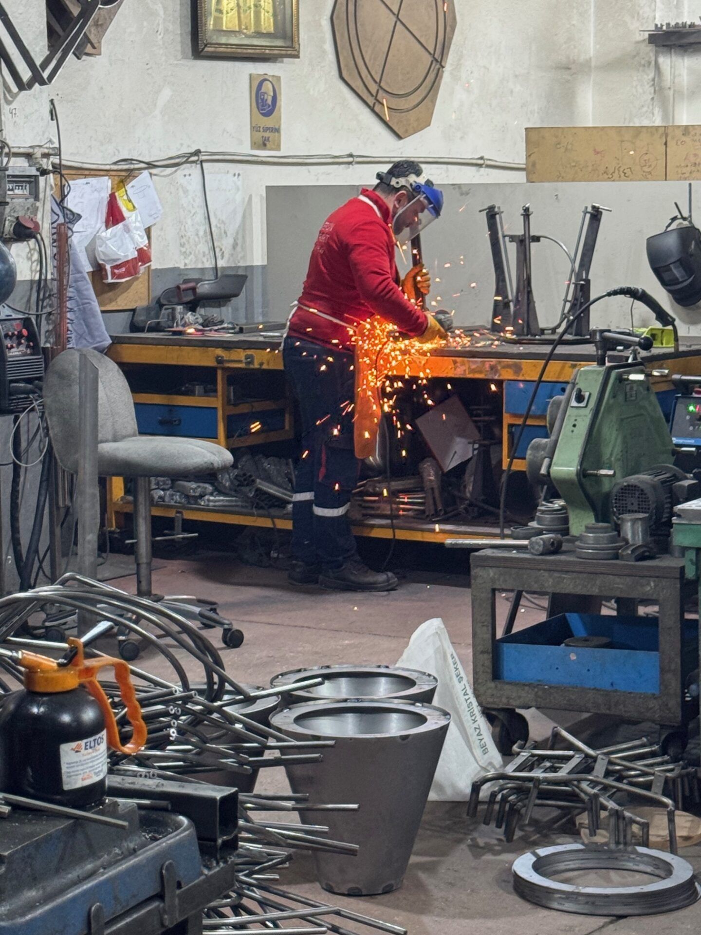 Metalworker grinding furniture frames at Istanbul Furniture Fair, sparks flying. Focus on design and craftsmanship.