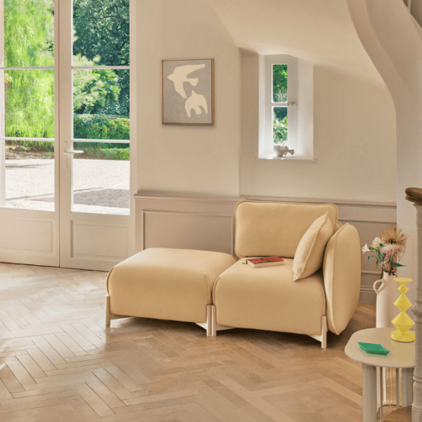 Angled view of a Linka Corner Sofa in cream upholstery with metal frame in a bright, modern living space.