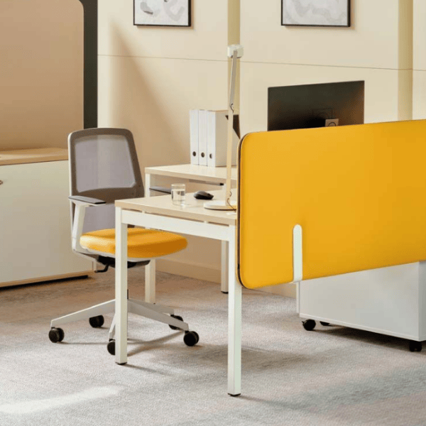 Angled view of a yellow Sonic Sit Stand Desk Screen attached to a desk, with a white frame, acoustic nonwoven filling and fabric cover.