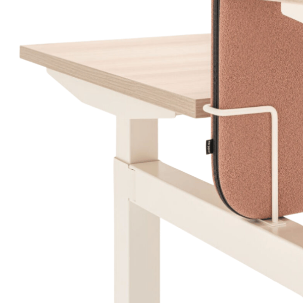 Close-up of a wood desk with a cream metal frame & a rose-colored fabric Sonic Sit Stand Desk Screen attached to its side.
