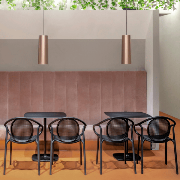 Modern interior featuring two bronze 'To Be' pendant lights above black tables and chairs, complemented by a plush pink banquette.