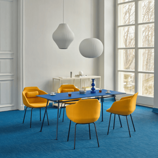 Angled view of the Ultra Armchair in yellow upholstery with a wooden frame, part of a modern dining set with a blue table.