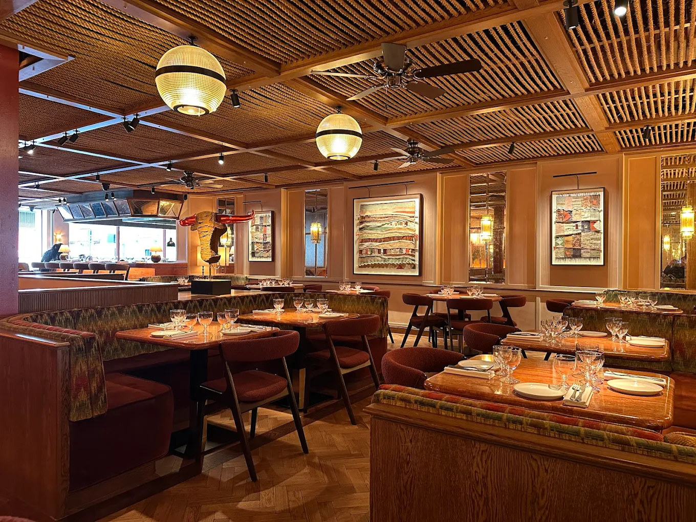 Kudu Marylebone restaurant interior. Tables set for diners in a warmly lit, stylish South African dining room, banquette seating, restaurant furniture.