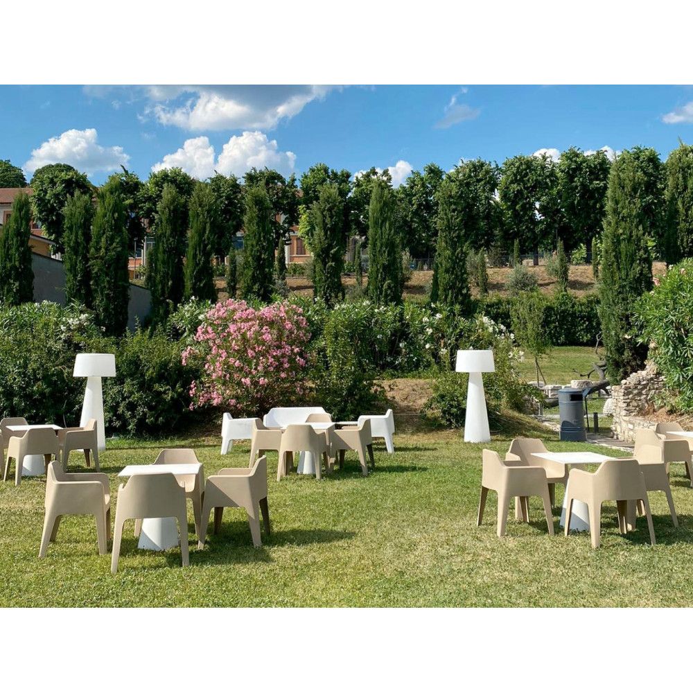 Outdoor setting featuring a neutral Time Out Floor Lamp, tables, and chairs on a green lawn with trees and sky in the background.