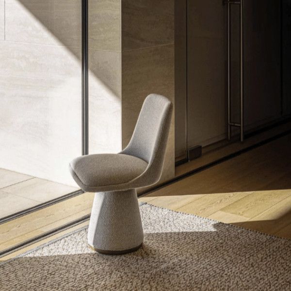 Angled view of a gray upholstered Flo Side Chair with a unique pedestal base, sitting on a patterned rug in a modern interior.