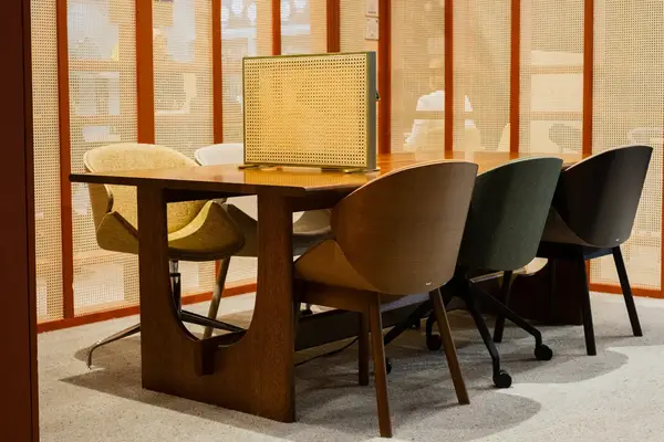 Angled view of a Sund Dining Table with a brown wooden top and base, surrounded by several stylish, colorful chairs.