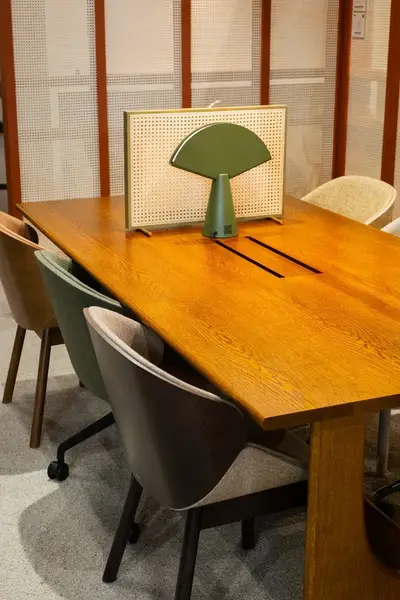 Angled view of the Sund Dining Table, featuring a wooden top and modern chairs. Table has a green lamp and a screen on top.