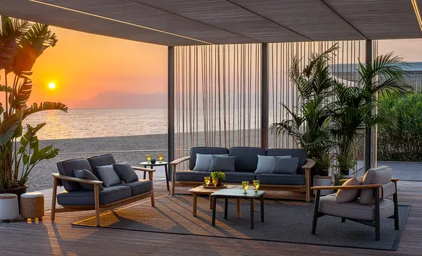 The Twins Sofa in an outdoor setting, featuring a metal frame, wooden armrests, and upholstered cushions, designed for elegant and durable outdoor seating.