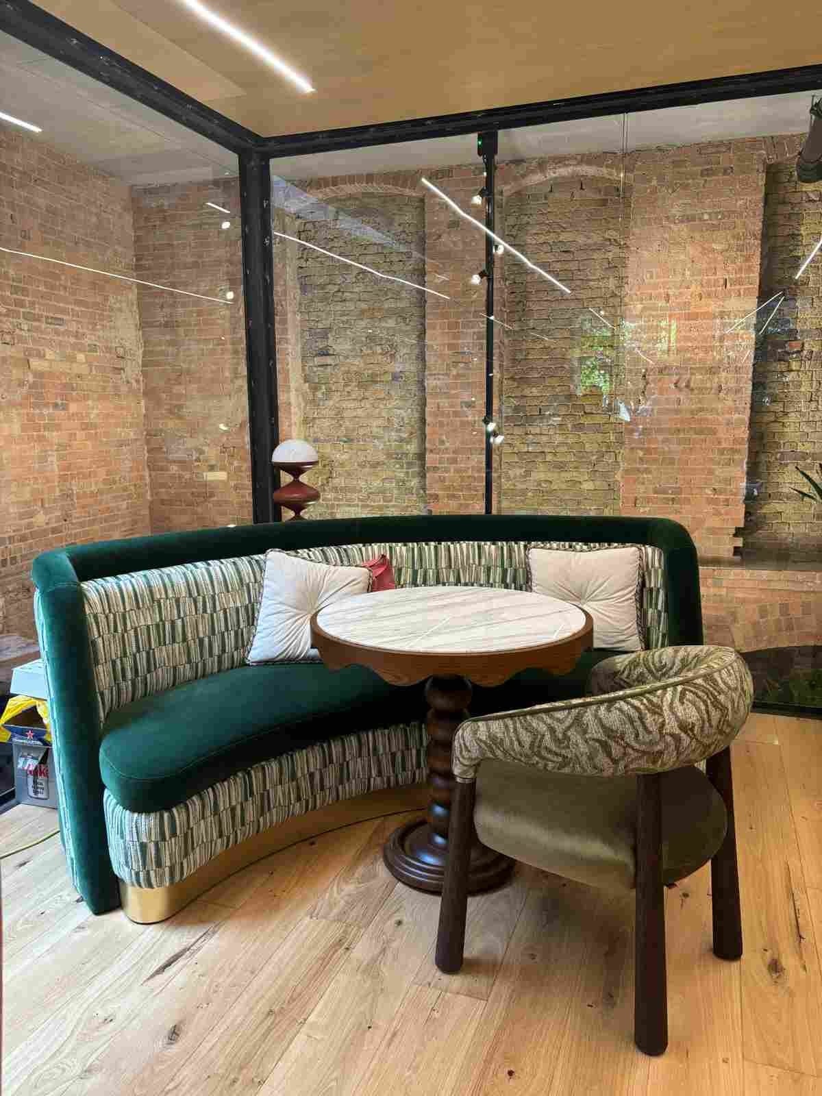 Green banquette seating with patterned upholstery, round marble-topped table, and patterned chair sit on a wood floor.