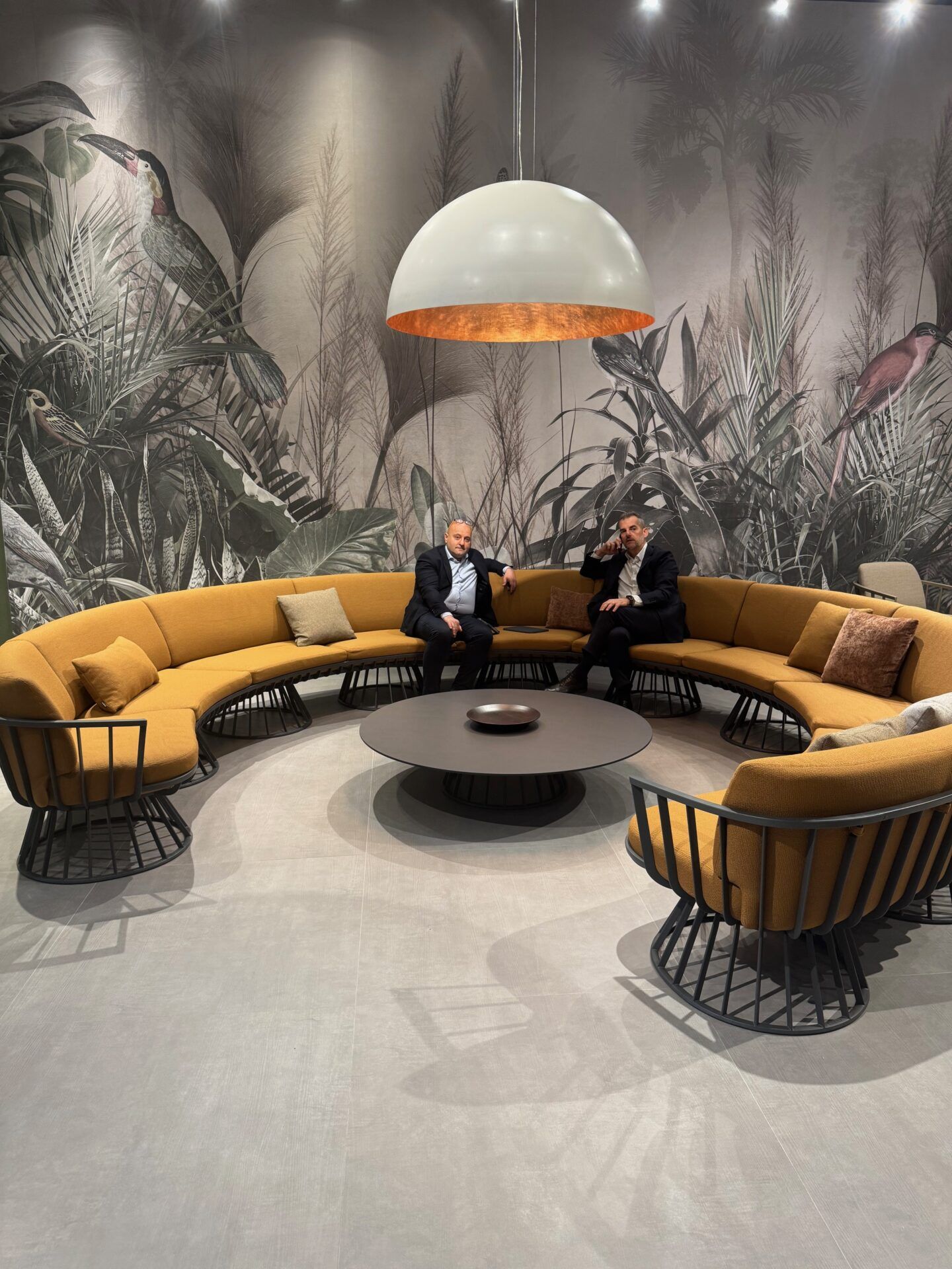 Salone del Mobile 2026 hospitality trends: Stylish yellow lounge seating with men, tropical wallpaper, and modern lighting.