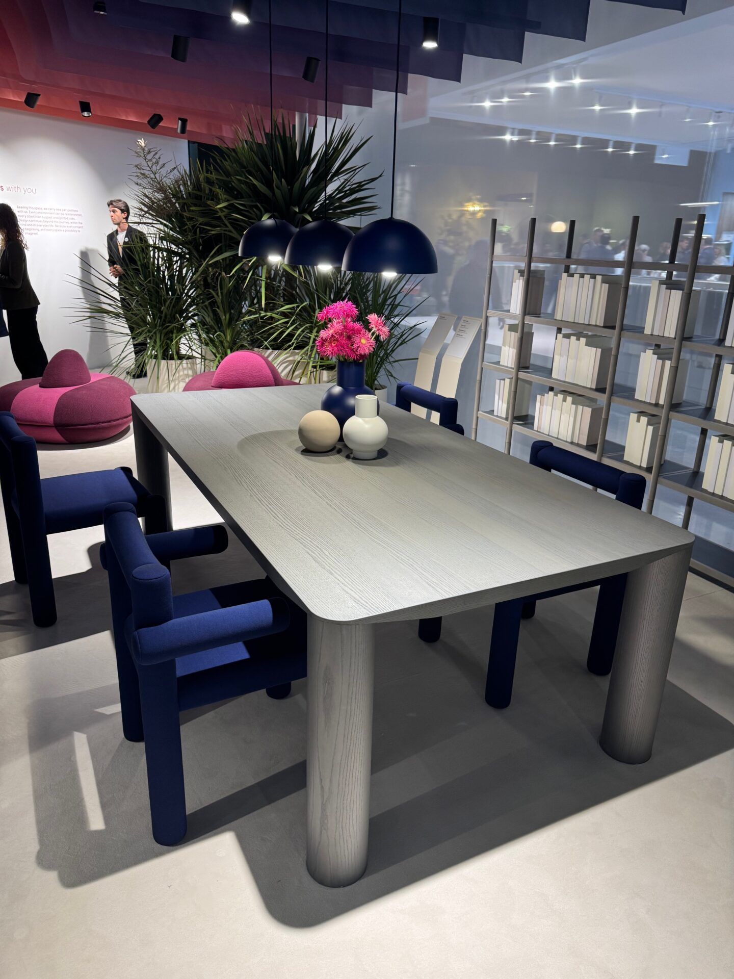 Salone del Mobile 2026 hospitality trend: Modern dining table with unique blue chairs, featuring a floral centerpiece.