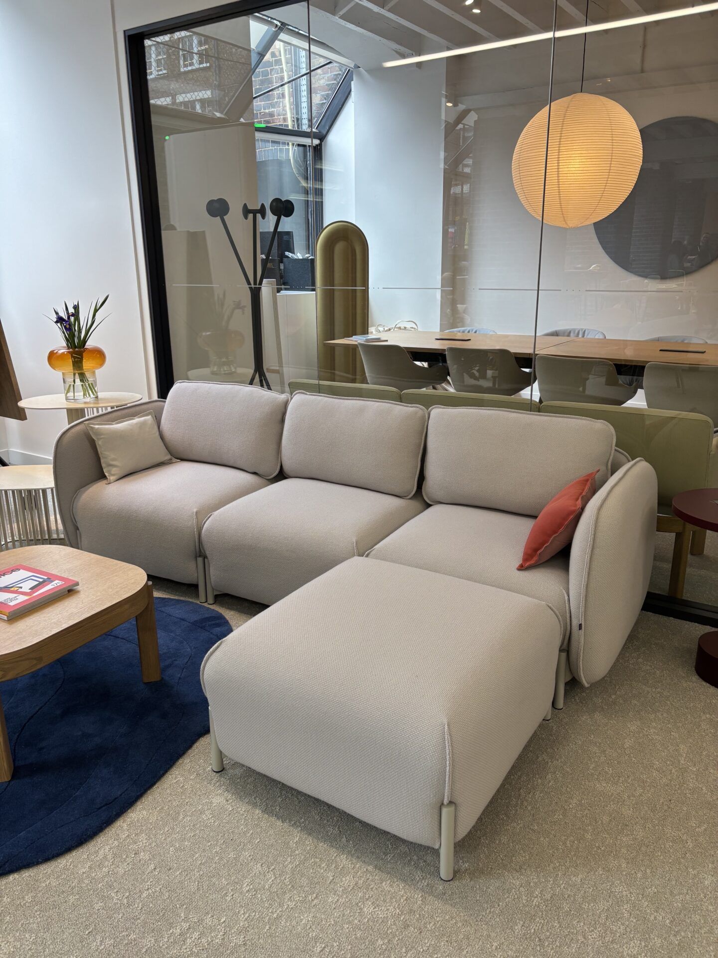 Modular sofa with off-white textured cushions and a small coral pillow rests on a blue rug in a showroom.