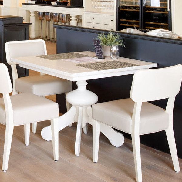 Foreground showcases the Marie Column Dining Table, featuring a bright, square tabletop, ornate pedestal base, and seating for three.