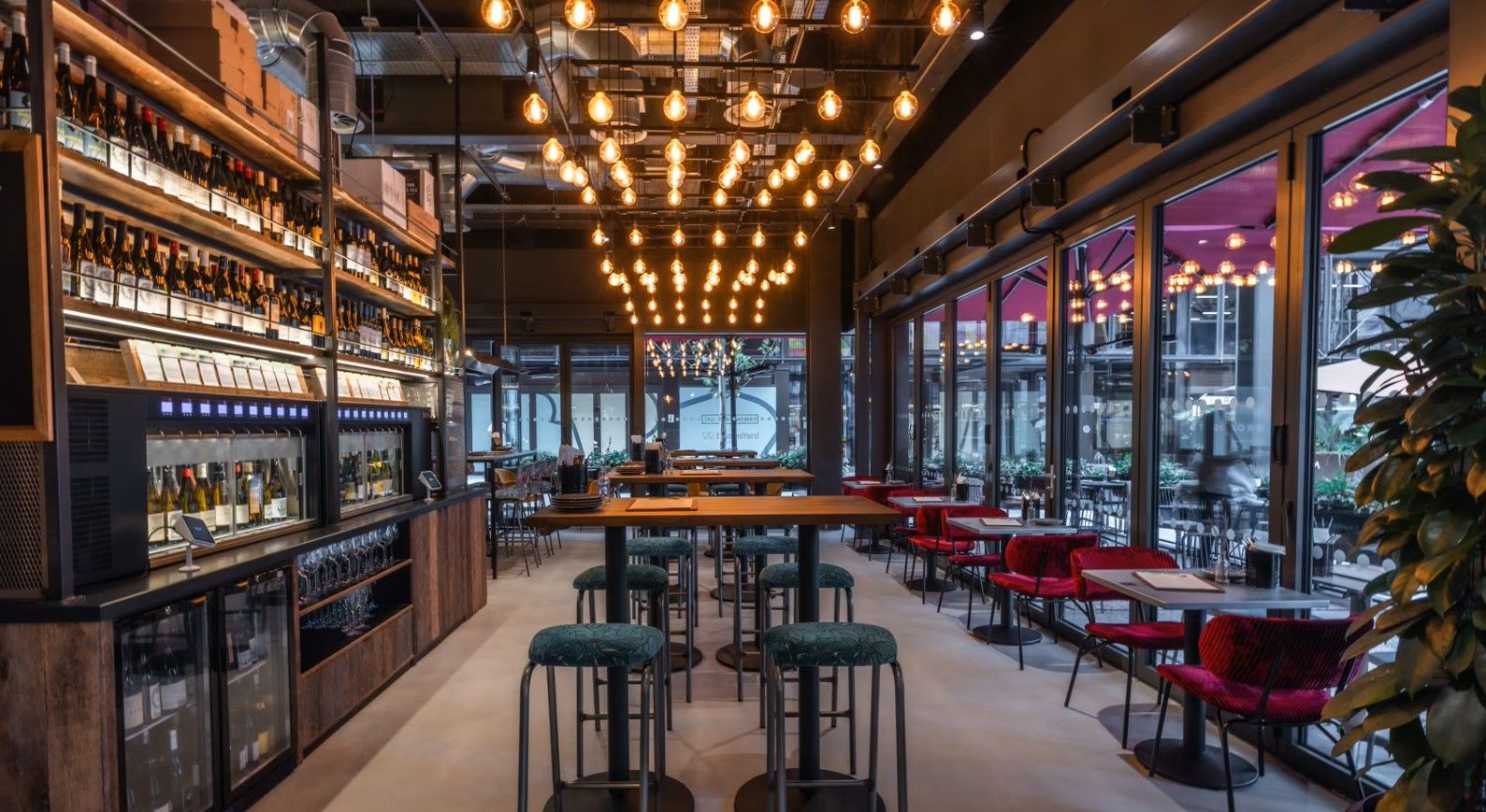 Vagabond Broadgate1 In a restaurant, the Caldas Coffee Table, with a wood top, is showcased amidst barstools and overhead lighting fixtures.