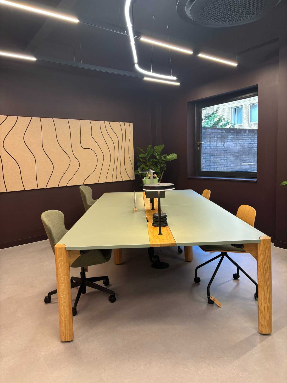 Long pale green conference table with oak legs sits in a dark room under linear LED lights.