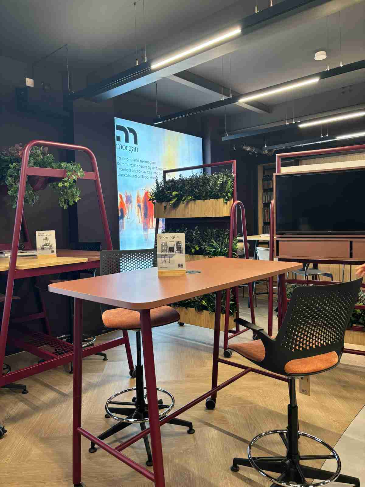 Tall desk with a rust-colored top and a black and rust office chair face a screen displaying the Morgan logo and information.
