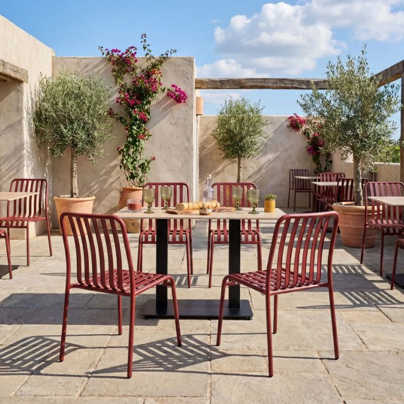 Foreground features the Henley Side Chair's metal frame in a rich red hue, complemented by a slatted seat and back, perfect for outdoor settings.