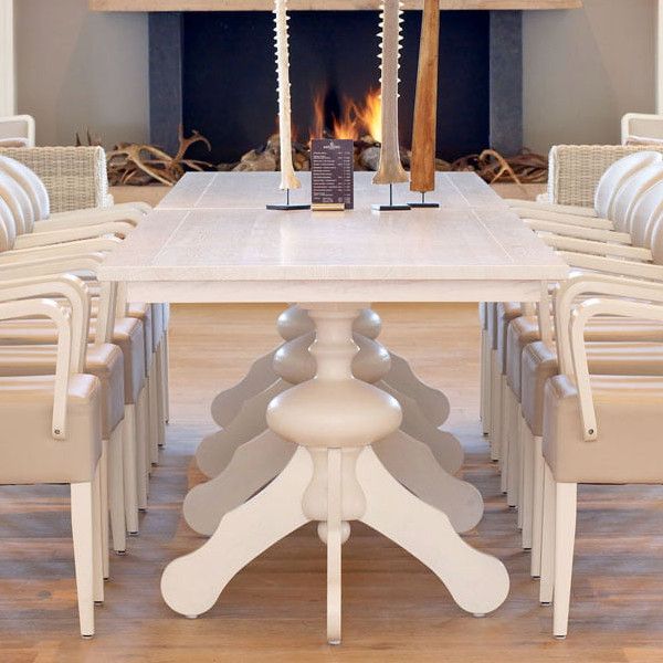 Captured straight-on, the Marie Column Dining Table showcases a light wood finish, complementing the chairs around it. A cozy fireplace is in the background.