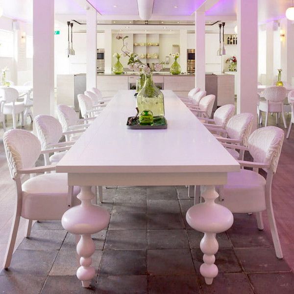 Centered shot displays a white Marie Rectangle Dining Table with unique turned legs and matching chairs, set in a bright restaurant interior.