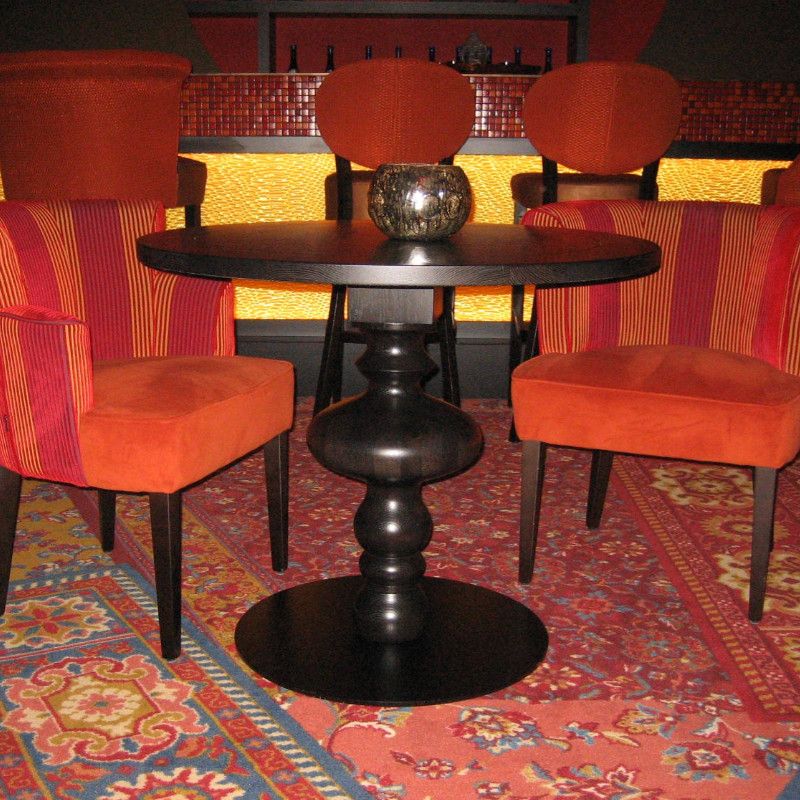 Behold the Marie Round Dining Table: a dark wood table with a unique, sculpted pedestal base, paired with orange striped chairs.