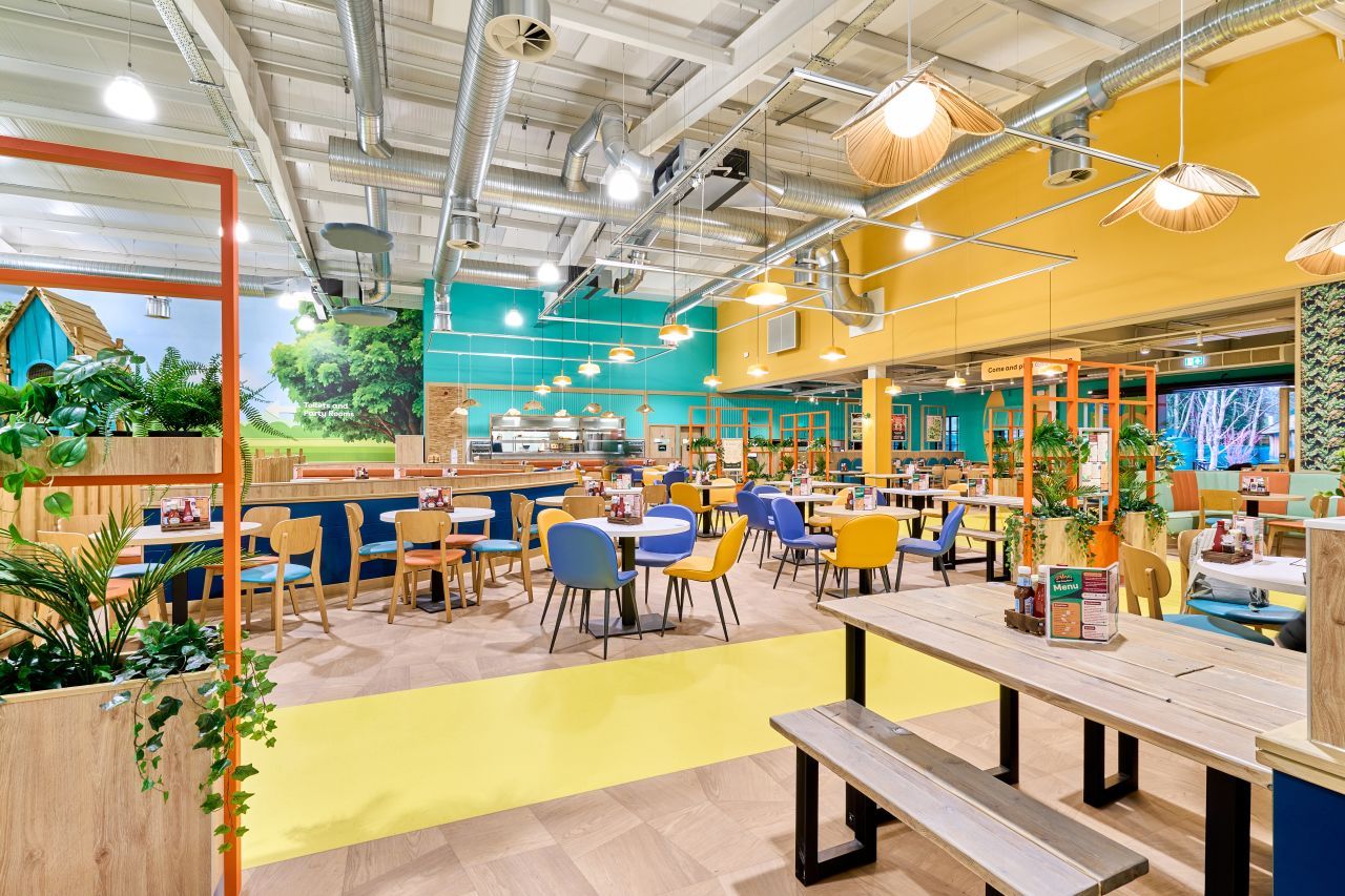 Birdworld7 Colorful Merinal lounge chairs arranged in a bright, modern commercial space with yellow accents and wooden tables.