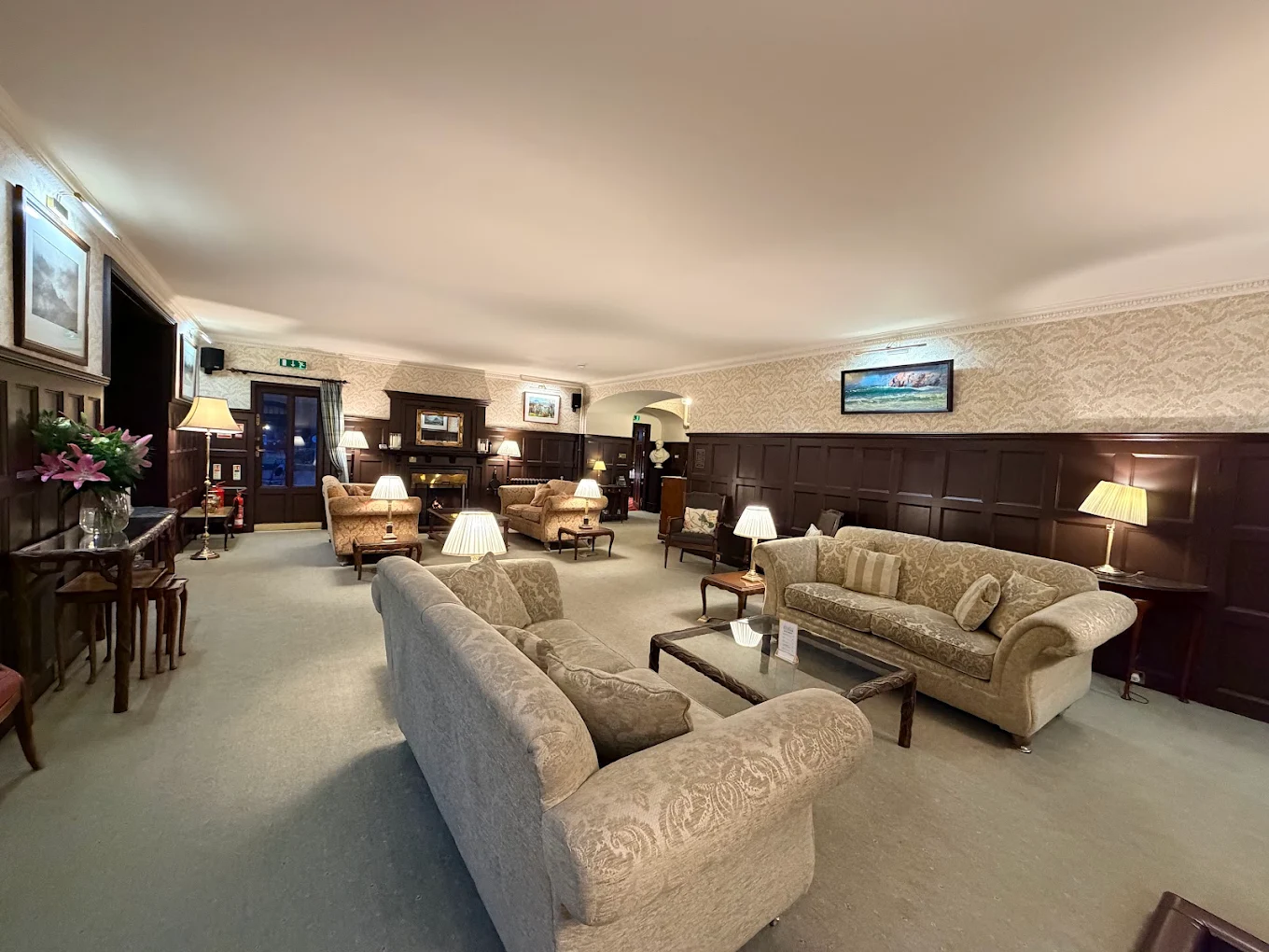 Bunchrew House1 Patterned beige upholstered sofas positioned around glass coffee tables within a wood-paneled hotel lounge.