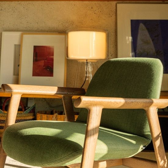 Ekuru lounge chair in forest green upholstery with a natural wood frame, bathed in warm sunset light indoors.