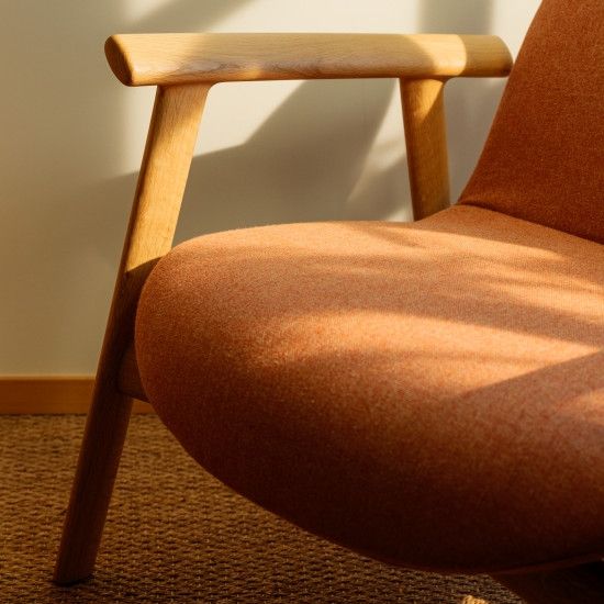 Close-up view of the Ekuru lounge chair showcasing its textured rust-orange fabric and smooth light timber armrest.