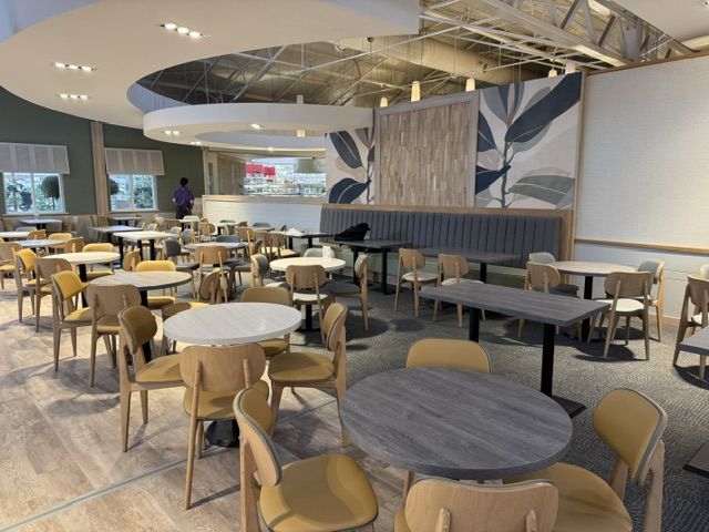 Modern restaurant dining area with circular and rectangular tables, light wood chairs with mustard cushions, and booths.