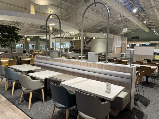 Haskins Garden Centre Spacious restaurant interior featuring grey upholstered banquette seating partitioned by tall arched metal frames.