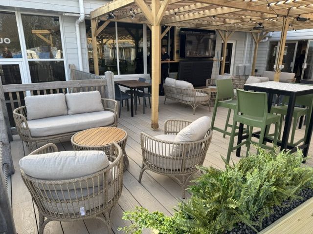 Hoburne Bashley Holiday Park Wicker armchairs and a matching sofa arranged on a grey wooden deck under a timber-framed patio canopy.