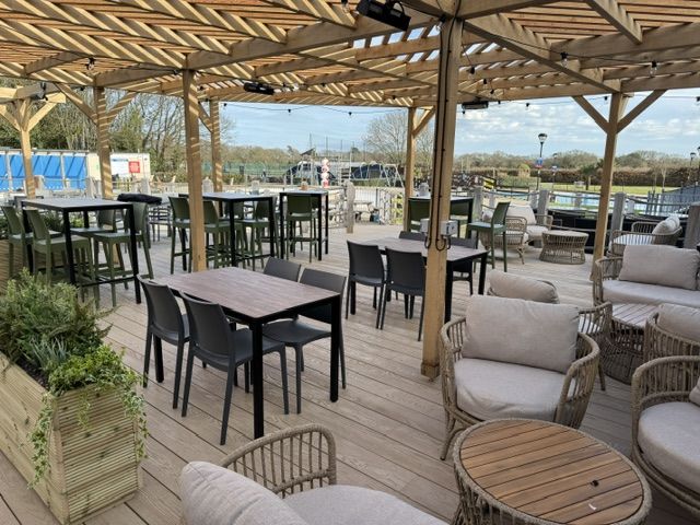 Outdoor wooden pergola covering a deck with dining tables, chairs, and lounge seating at Hoburne Bashley Holiday Park.