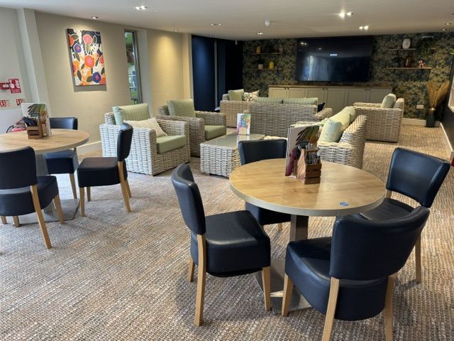 Round wooden tables paired with dark blue chairs sit before a lounge area furnished with light wicker armchairs.